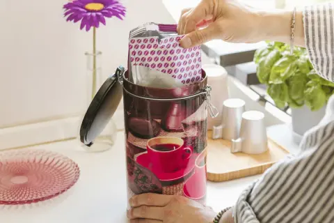 Contenitore decorato per conservare il caffè macinato, con pacchetto di caffè in mano.