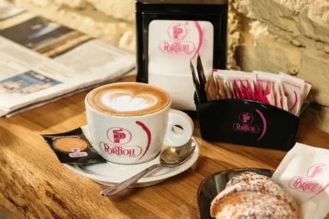 Un cappuccino perfetto con schiuma a forma di cuore, accompagnato da un croissant e un giornale.