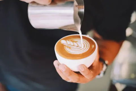 Un barista crea un disegno a latte art su un cappuccino. Latte art: cappuccino prima latte o caffè?