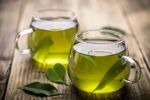 Due tazze di tè verde, con foglie fresche immerse, pronte per gustare le loro proprietà benefiche.