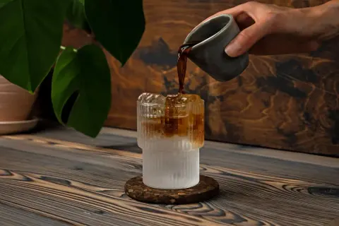 Versando caffè in un bicchiere con ghiaccio e acqua frizzante. Un'idea rinfrescante per l'estate.