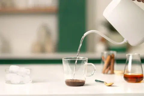 Preparazione di un delizioso spanish latte: acqua calda versata su caffè, cubetti di ghiaccio e un tocco di dolcezza.