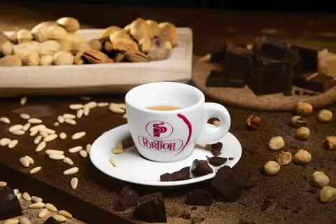 Tazza di caffè fumante, circondata da pezzi di cioccolato fondente, nocciole e pinoli. Un'invitante combinazione di caffè e cioccolato.