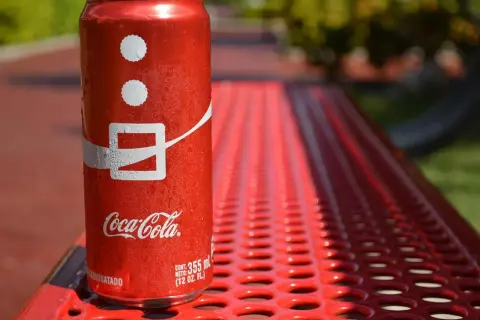Lattina di Coca-Cola su panchina rossa, con gocce d'acqua. Attenzione, la Coca-Cola fa alzare la pressione!
