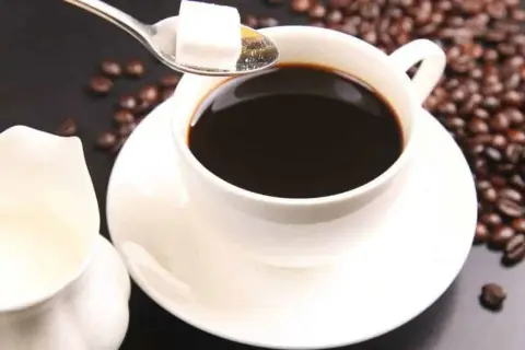 Un caffè americano al bar, con chicchi tostati e zollette di zucchero su un cucchiaino.