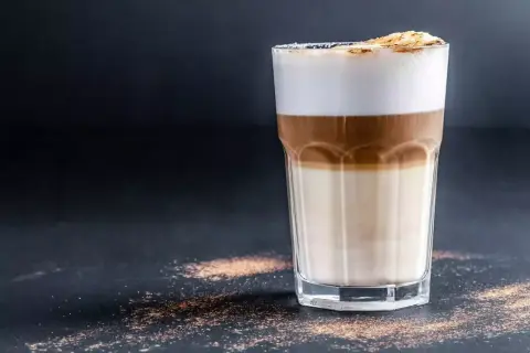 Un bicchiere di latte macchiato con strati distinti di latte, caffè e schiuma. Ecco come si fa, un piacere visivo e gustativo.