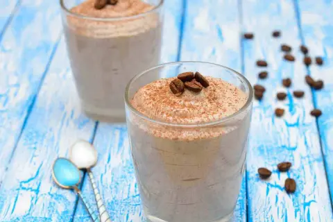 Delizioso sorbetto al caffè ricetta, guarnito con chicchi di caffè e cacao, servito in bicchieri su un tavolo di legno blu.