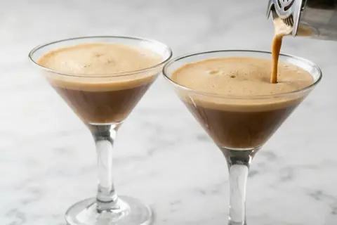 Due bicchieri di caffè shakerato cremoso, uno viene riempito da uno shaker.