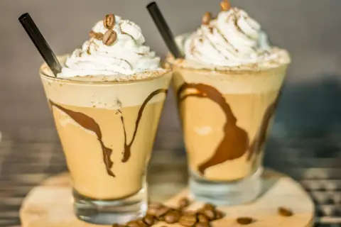 Due deliziosi milkshake al caffè, guarniti con panna montata, chicchi di caffè e sciroppo al cioccolato, pronti per essere gustati.