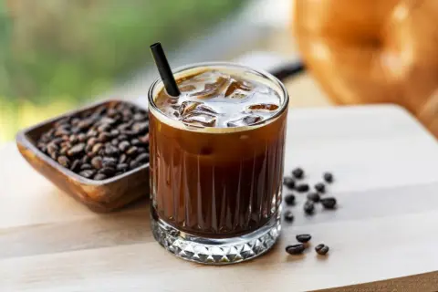Un bicchiere di caffè freddo, con ghiaccio e cannuccia, accanto a chicchi di caffè. Ecco cos'è il cold brew: una bevanda rinfrescante.