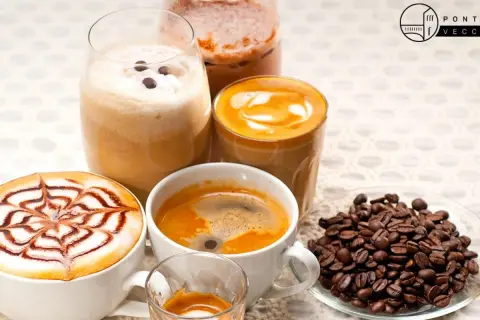 Varietà di deliziosi caffè italiani: un espresso, un cappuccino decorato, un caffè macchiato e un frappé. Chicchi di caffè tostati completano la scena.