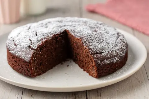 Una deliziosa torta caffè e cioccolato fondente, cosparsa di zucchero a velo, con una fetta mancante.