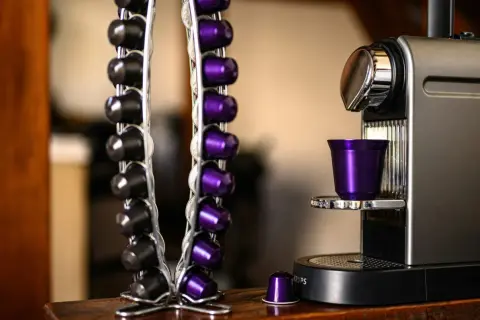 Macchina caffè Caffitaly con spia rossa lampeggiante. Capsule nere e viola in un portacapsule accanto.