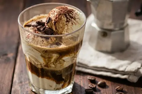Un delizioso gelato affogato al caffè, guarnito con scaglie di cioccolato e cacao, pronto per essere gustato.
