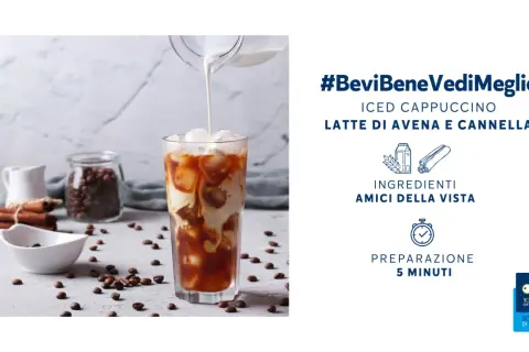 Un rinfrescante cappuccino di avena freddo versato in un bicchiere con ghiaccio, circondato da chicchi di caffè e cannella.