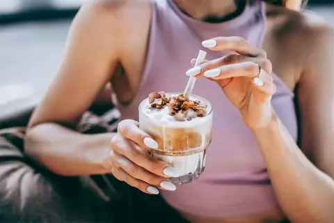 Mani con unghie bianche sorreggono un bicchiere di delizioso **caffè freddo** con topping croccante.