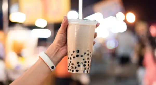 Un bicchiere di bubble tea con perle nere, tenuto da una mano con un braccialetto bianco. Un sorso di freschezza che ricorda le sue origini asiatiche.
