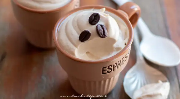 Deliziosa ricetta crema caffè con panna, guarnita con chicchi di caffè, servita in tazzine su un tavolo di legno.