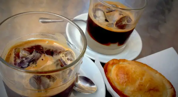 Due caffè salentino con ghiaccio e una pastarella su un tavolino.