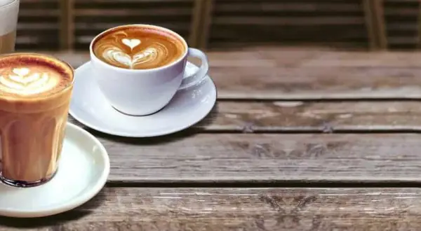 Due tazze di caffè con schiuma decorata, una in bicchiere e una in tazza bianca. Illustrano la differenza tra latte macchiato e caffelatte.