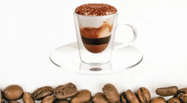 Un bicerin coffee a strati in una tazza di vetro, con cacao in polvere in cima e chicchi di caffè tostati sul fondo.