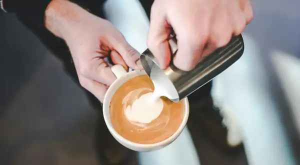Barista versa latte montato in una tazza di caffè, creando un disegno a spirale.