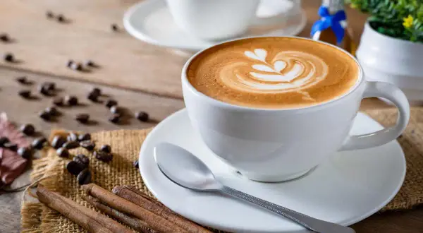 Tazza di cappuccino con latte art, chicchi di caffè e cannella. Nonostante la sua bellezza, la schiuma del cappuccino fa male se consumata in eccesso.