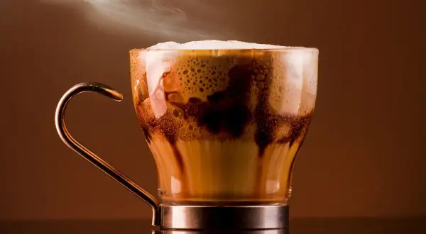 Un delizioso marocchino bevanda fumante in una tazza di vetro trasparente, con schiuma cremosa e striature di cioccolato.