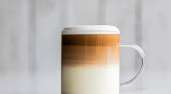 Un bicchiere di caffè macchiato caldo con strati distinti di latte e caffè, sormontato da una schiuma soffice.