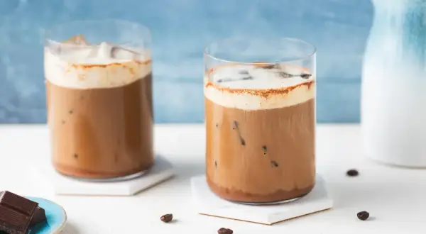 Due bicchieri di caffè freddo con schiuma e cacao, perfetti per una ricetta estiva.