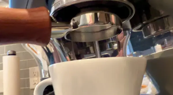 Manuale per capire come mettere le cialde nel portafiltro, con una tazzina bianca pronta a ricevere l'espresso.