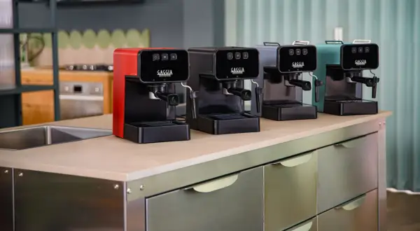 Macchine da caffè Gaggia in vari colori, una rossa, una nera, una grigia e una verde acqua, disposte su un bancone. Speriamo che la macchina caffè Gaggia non esca il caffè, altrimenti la colazione è rovinata!