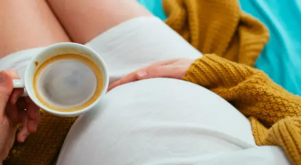 Mom-to-be enjoys a moment of peace with a cappuccino, resting her hand on her belly.