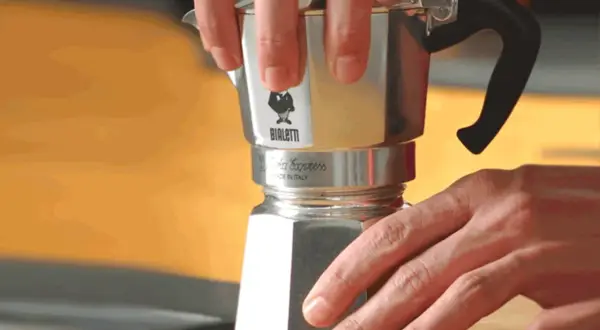 Mani che smontano una moka Bialetti per pulirla dal calcare. Un gesto semplice per un caffè perfetto.