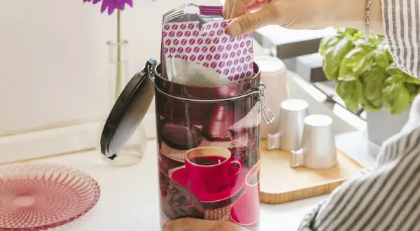 Contenitore decorato per conservare il caffè macinato, con pacchetto di caffè in mano.