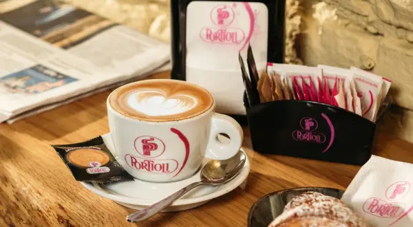 Un cappuccino perfetto con schiuma a forma di cuore, accompagnato da un croissant e un giornale.