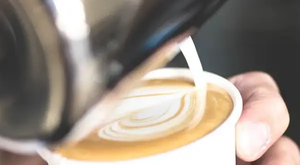 Un barista crea un cuore di latte art su un caffè. Il latte si monta caldo o freddo, creando una schiuma perfetta per il cappuccino.
