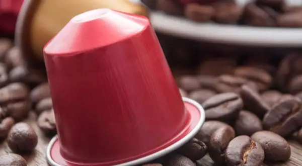 Una capsula di caffè rossa, circondata da chicchi di caffè tostati, pronta per un'esperienza aromatica.