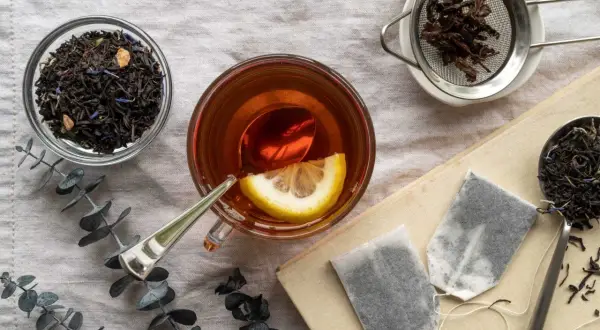 Tazza di tè Earl Grey con limone, foglie di tè sfuse e bustine. Scopri i benefici del tè Earl Grey per il tuo benessere.