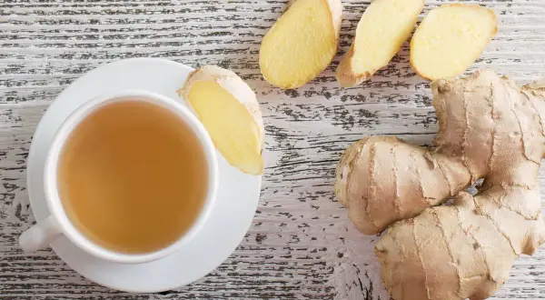 Tazza di tè allo zenzero, con radici e fette di zenzero fresco. Scopri i benefici dello zenzero per il tuo benessere.