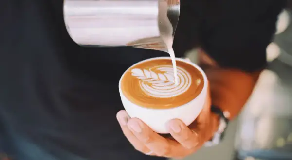 Un barista crea un disegno a latte art su un cappuccino. Latte art: cappuccino prima latte o caffè?