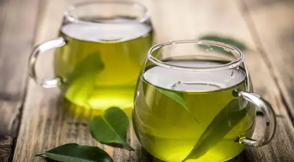 Due tazze di tè verde, con foglie fresche immerse, pronte per gustare le loro proprietà benefiche.