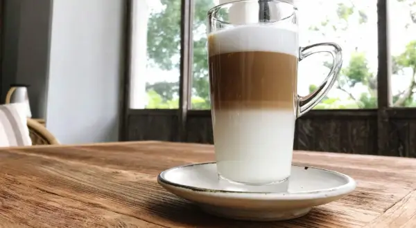 Un macchiatone, un caffè stratificato in un bicchiere trasparente, su un tavolo di legno rustico.