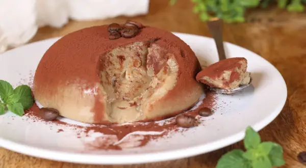 Delizioso budino al caffè, cosparso di cacao e chicchi di caffè, con una fogliolina di menta fresca.