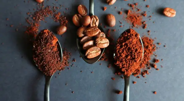 Tre cucchiai: uno con chicchi di caffè, gli altri due con la dose caffè per una tazzina, pronti per un'ottima colazione.