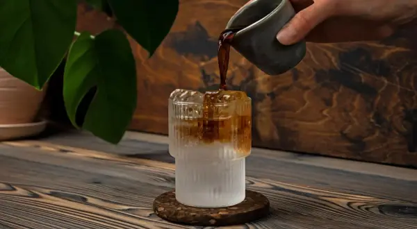 Versando caffè in un bicchiere con ghiaccio e acqua frizzante. Un'idea rinfrescante per l'estate.