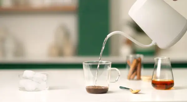 Preparazione di un delizioso spanish latte: acqua calda versata su caffè, cubetti di ghiaccio e un tocco di dolcezza.