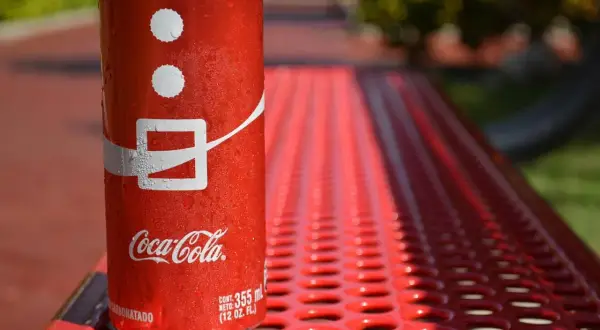 Lattina di Coca-Cola su panchina rossa, con gocce d'acqua. Attenzione, la Coca-Cola fa alzare la pressione!