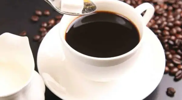 Un caffè americano al bar, con chicchi tostati e zollette di zucchero su un cucchiaino.