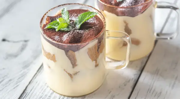 Delizioso monoporzione tiramisù in bicchiere, guarnito con cacao e menta fresca.